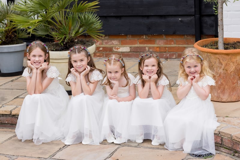 a row of flower girls in white dresses and headbands smiling at the camera.