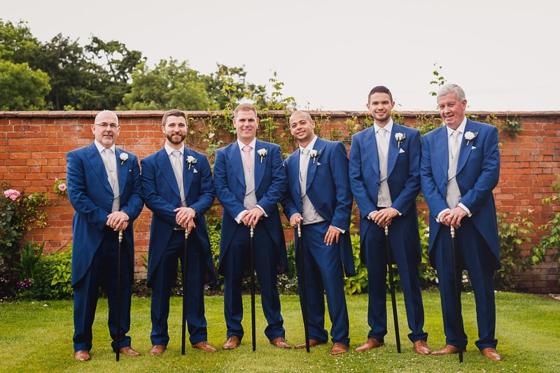 a group of groomsmen in blue morning suits for a wedding holding canes.