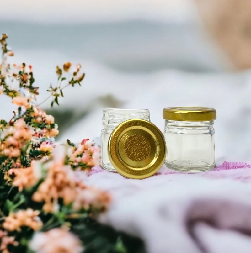 two miniature empty jam jars next to some flowers on a table.