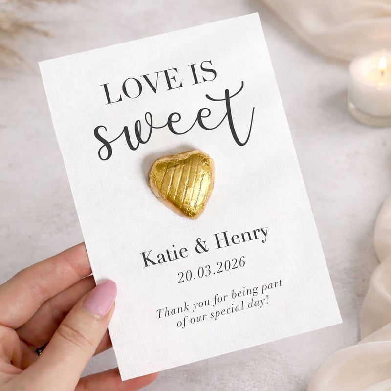 a hand holding a white card with gold-wrapped chocolate attached.
