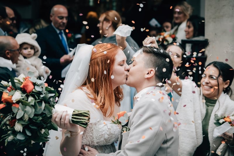 an LGBTQ+ couple kiss as guests throw confetti.
