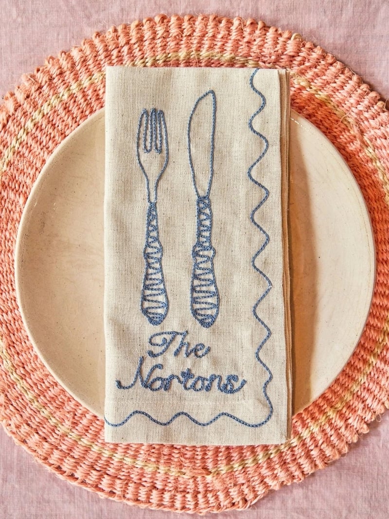 an embroidered linen napkin personalised with the words, 'the nortons' on a stripy place setting.