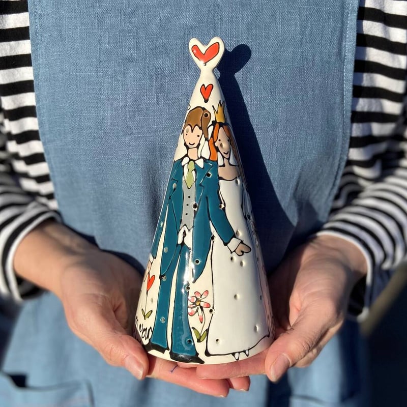 two hands holding a hand-painted cone-shaped tealight holder.