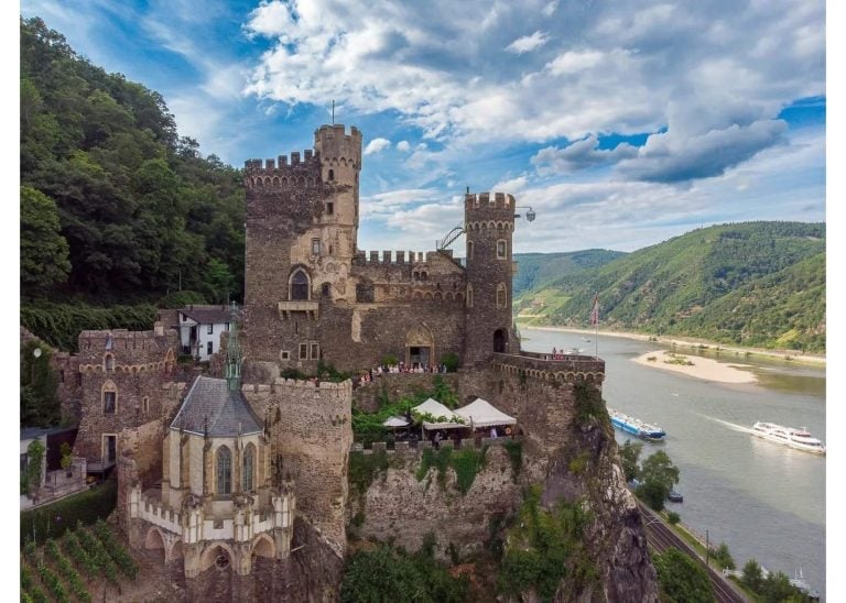 Mittelalterliche Burg auf einem Felsen über dem Rhein, im Hintergrund vorbeifahrende Schiffe