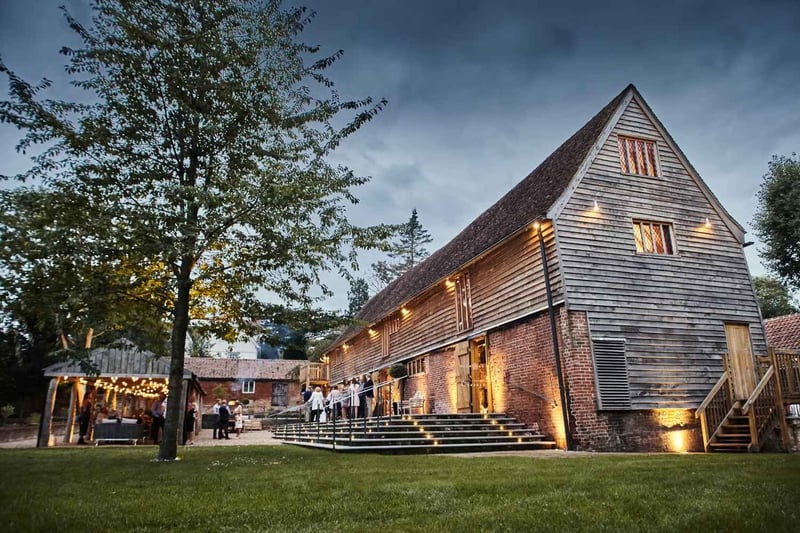 Timber-clad barn wedding venue exterior lit up with festoon lights at dusk