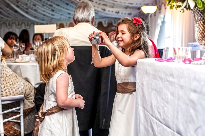 two flower girls play with a polaroid camera at a wedding reception.