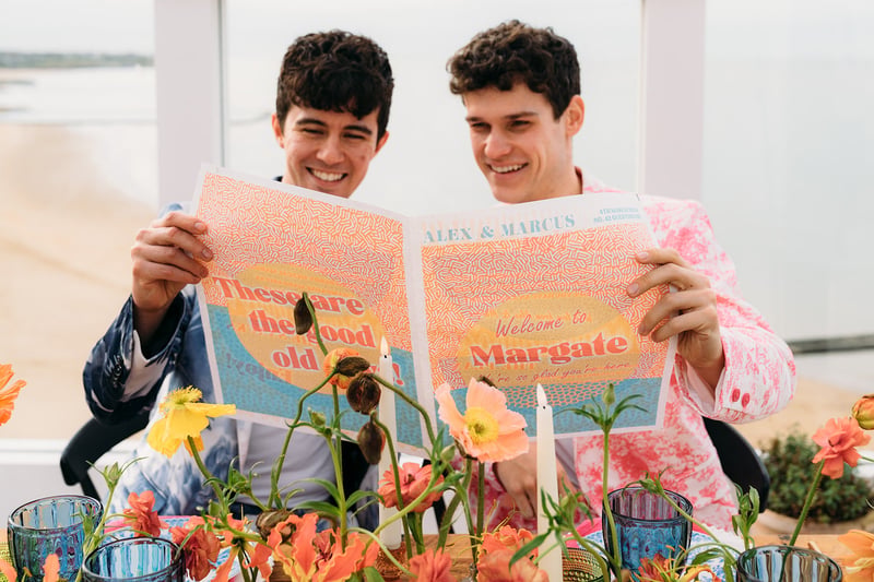 two grooms reading their wedding order of service newspaper.