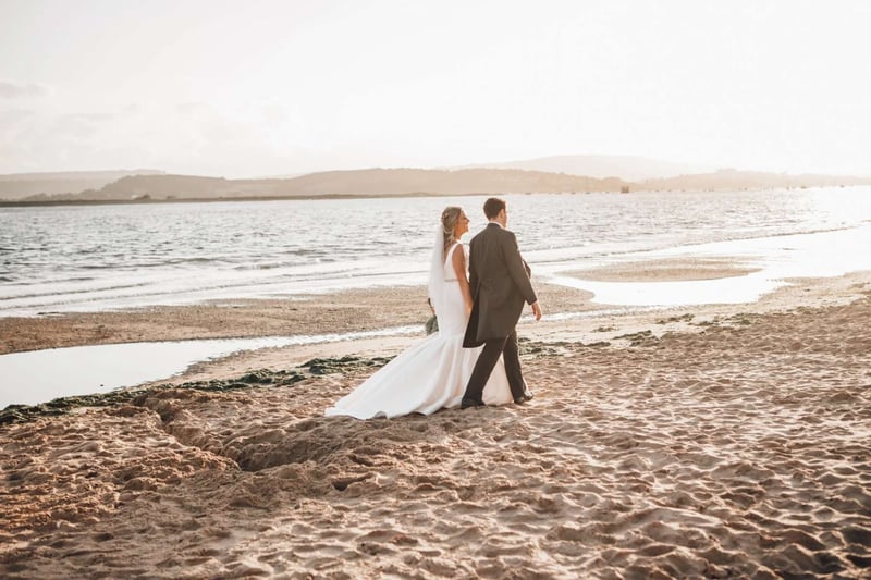 Bride and groom walking hand in hand along the sand at a beach wedding in devon