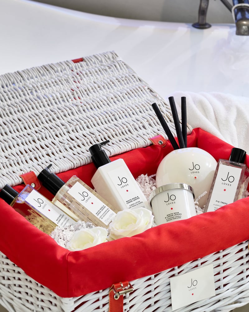 a white wicker hamper with red lining filled with fragrance items.