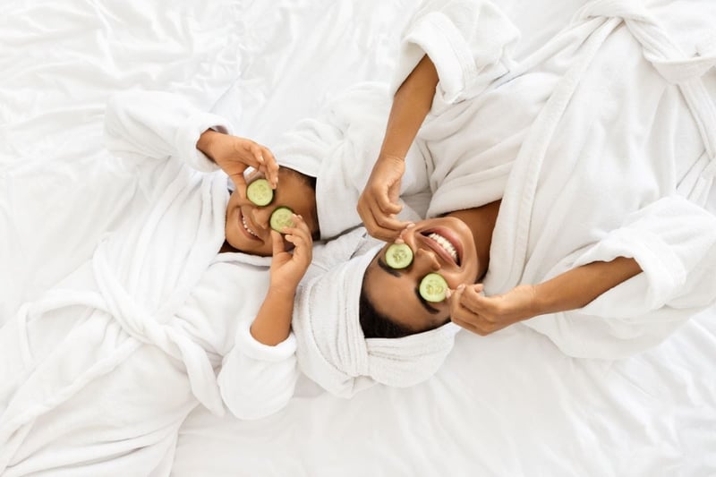 a mum and daughter in white dressing gowns and cucumber on their eyes having a spa day.