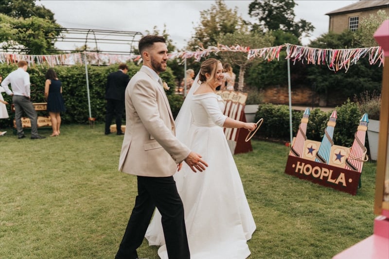 a newlywed bride and groom play vintage-style carnival games on the lawn of their wedding venue.