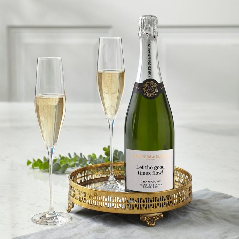 a bottle of champagne with personalised label on a tray next to two champagne flutes.