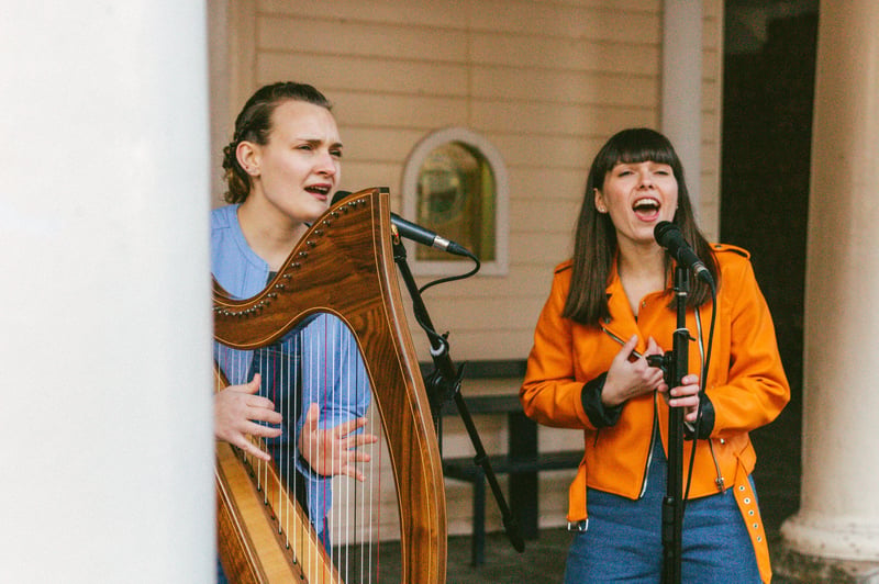 a harpist and vocalist perform together at an outdoor drinks reception.
