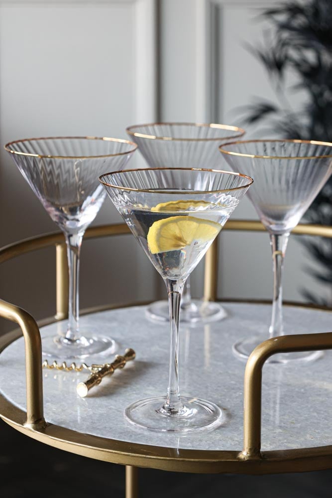 a set of four ribbed martini glasses with gold rim on a drinks trolley.