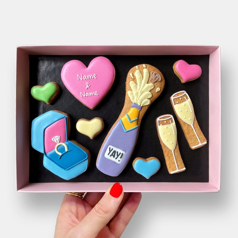 a hand holding a box of colourful iced biscuits in different shapes.