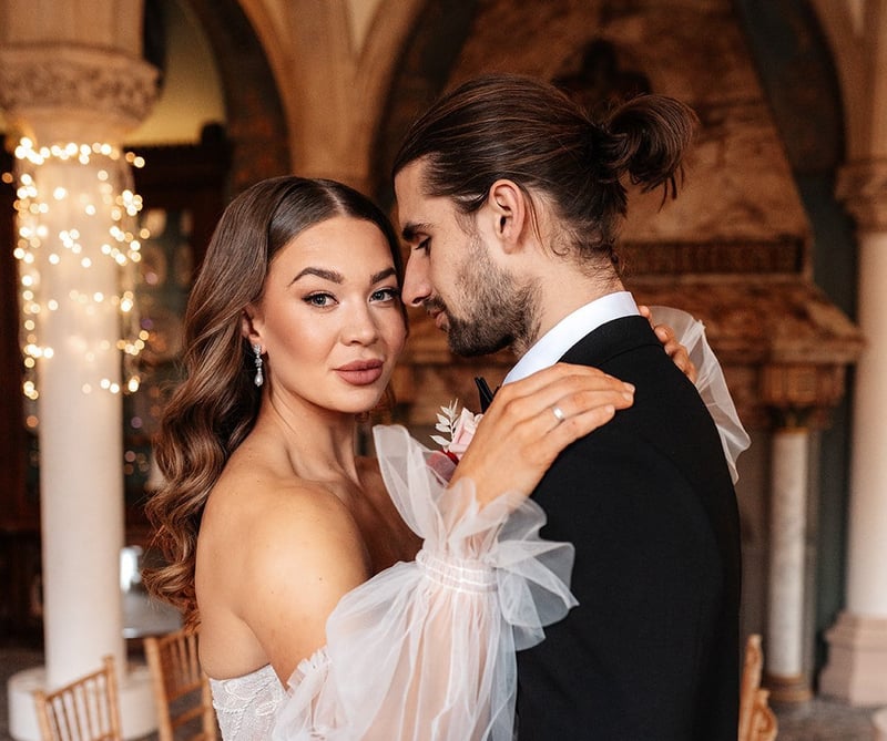 a bride with Hollywood style waves looks at the camera as she embraces her groom.
