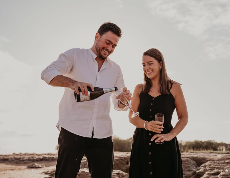 a man and woman pouring champagne on the beach. 