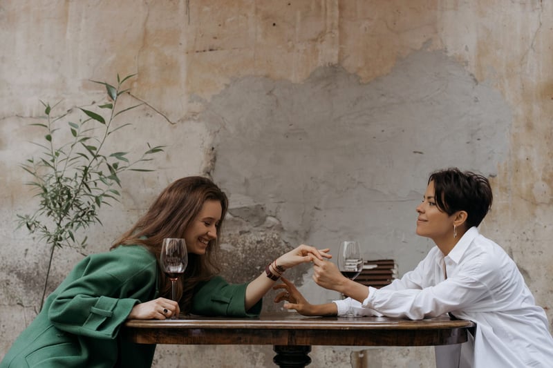 two women with wine holding hands over a table and smiling.