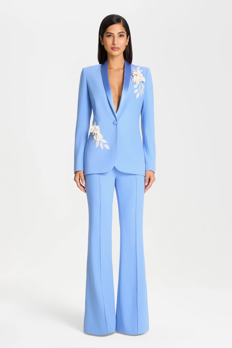 a model wears a light blue crepe mother of the bride trouser suit with white floral detail on the blazer.
