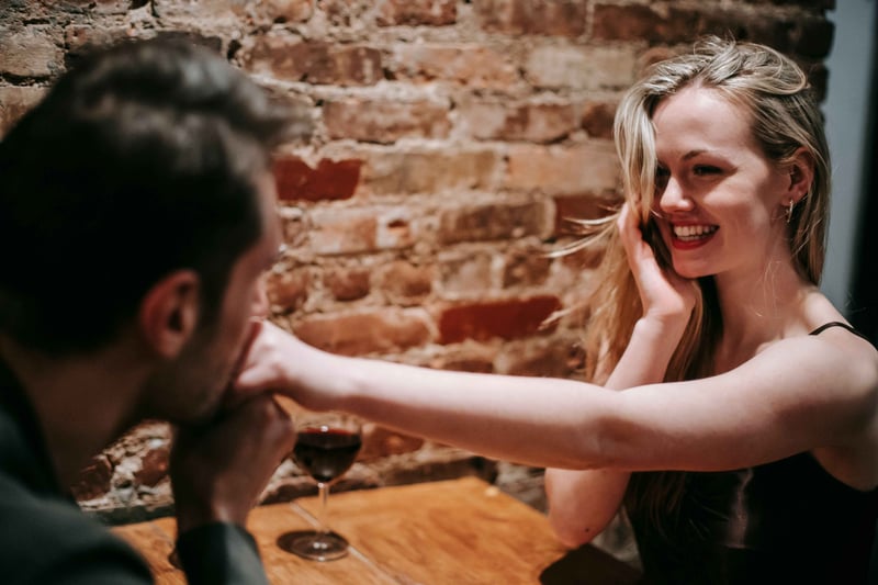 a woman in a wine bar smiling as a man kisses her hand.