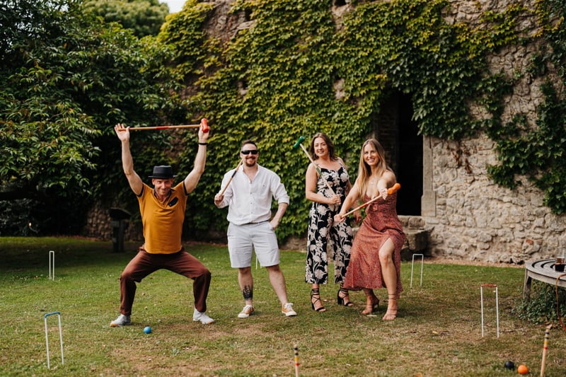 four party guests smile and celebrate as they play croquet outside.