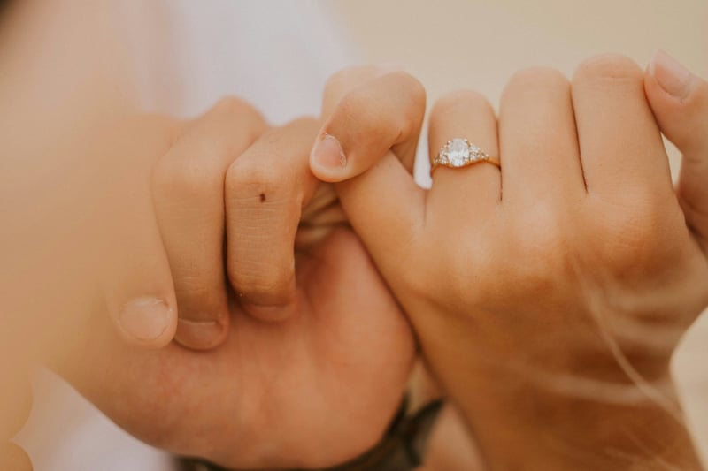 close up of two hands linking fingers, one is wearing an engagement ring.