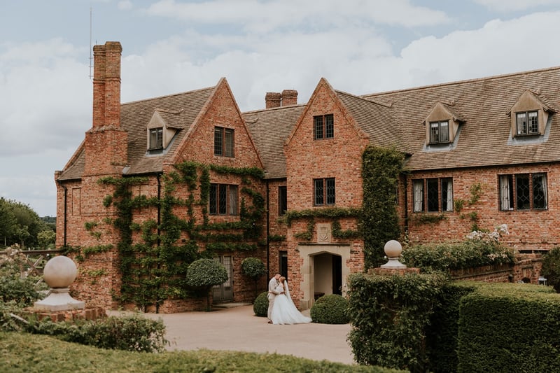 a newlywed bride and groom standing in front of a country house wedding venue.