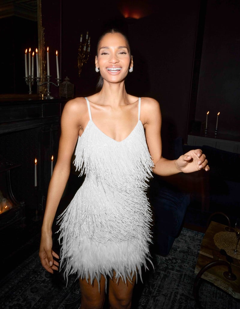 a model wears a beaded white mini dress and smiles at the camera.