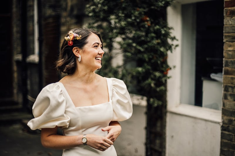 a bride with a short bob and flowers in her hair smiles in her wedding dress.