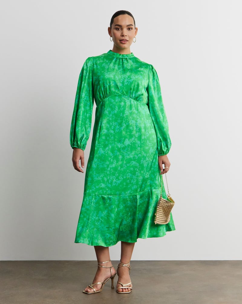 a plus size model wearing a green jacquard satin midi dress with high neckline and long sleeves.