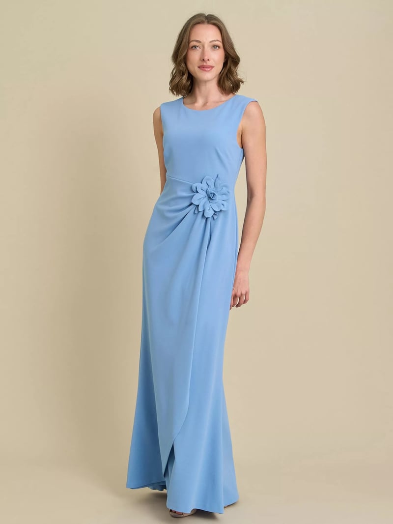 a model wears a pale blue sheath maxi dress with flower corsage detail at the waist.