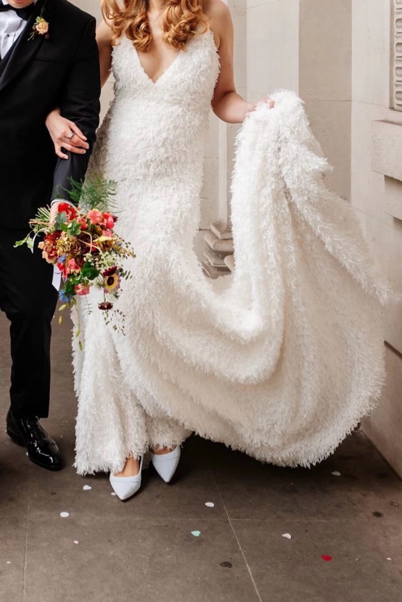 close up of a bride's faux feather wedding dress and bouquet as she stands with her groom.
