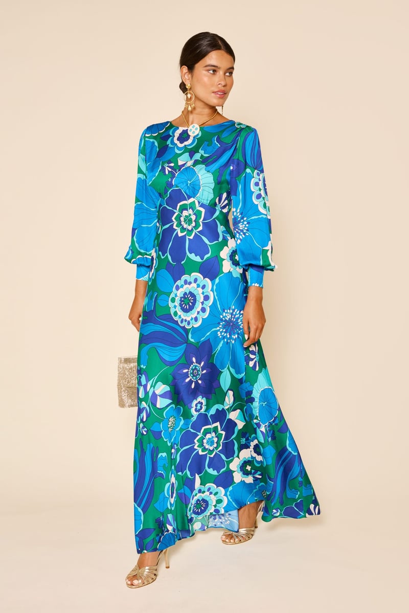 a model wears a blue and turquoise printed floral maxi dress with metallic sandals and handbag.