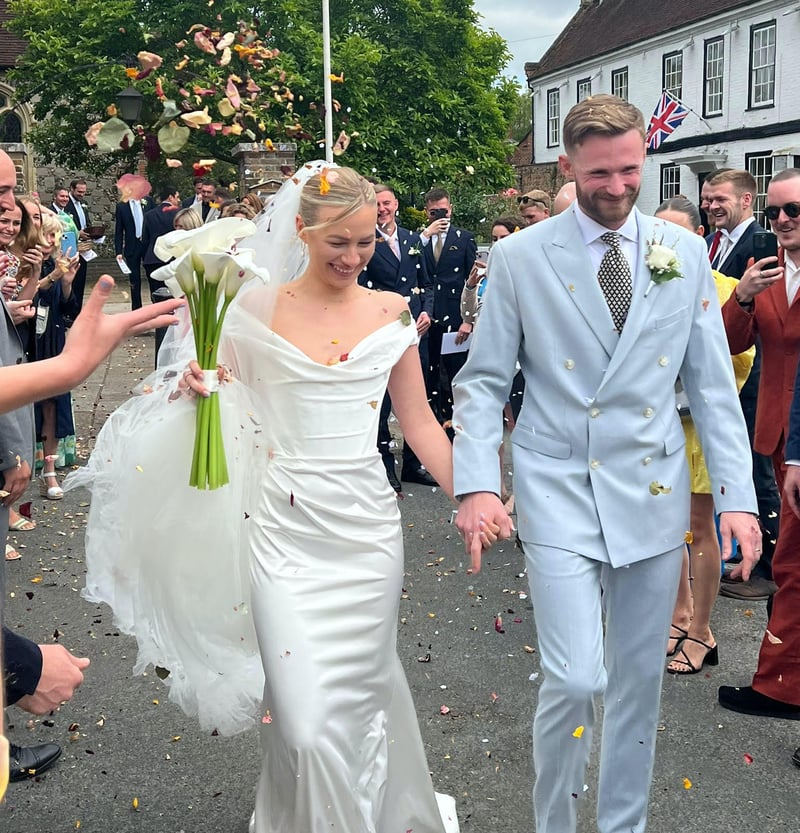 a bride wearing a hired wedding dress walks with her groom as guests throw confetti.