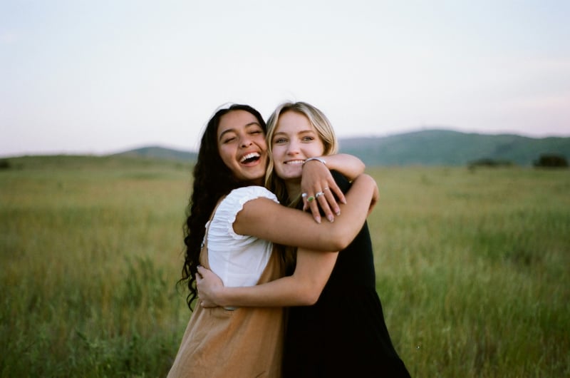 two women hugging in a field after engagement proposal.