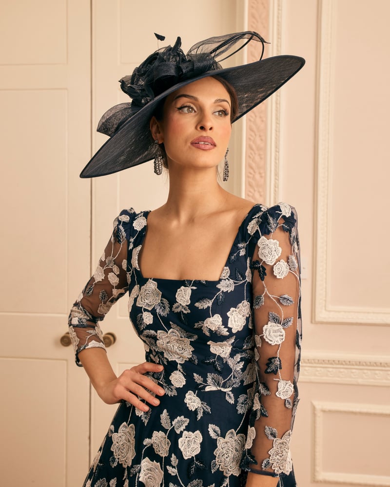 a model wears a black and white floral dress with sheer sleeves and a black hat.