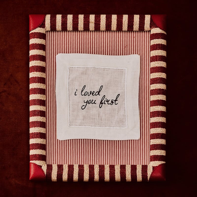 a handwritten embroidered linen coaster on a fabric frame.