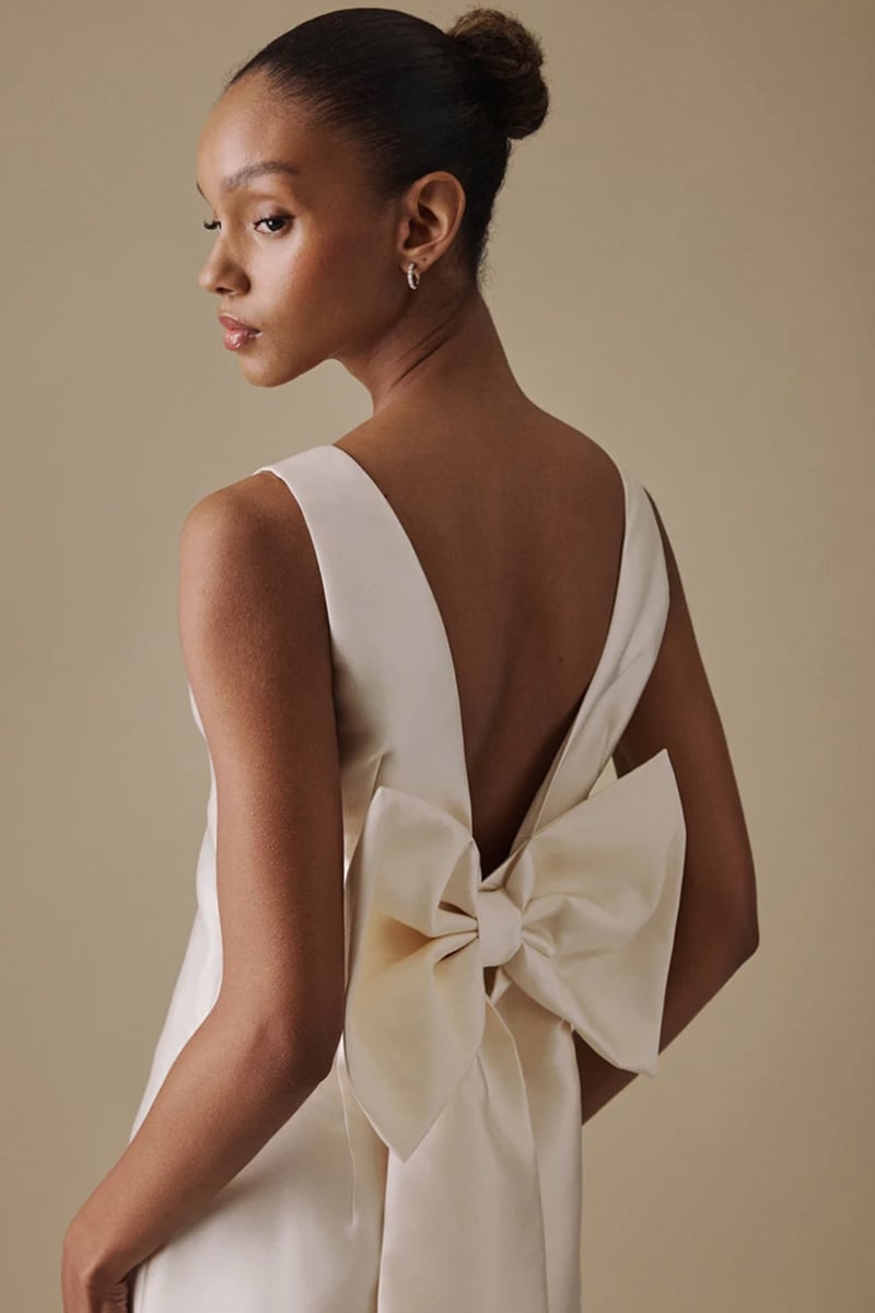 a model stands with her back to camera wearing a wedding dress with bow detail.