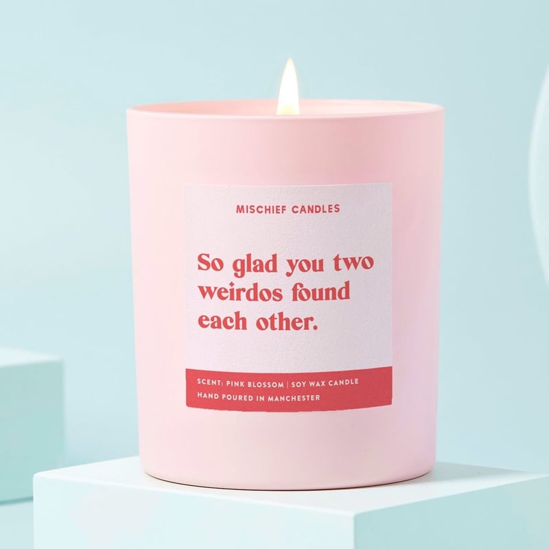 a pale pink candle with label that reads, 'so glad you two weirdos found each other' in red text.