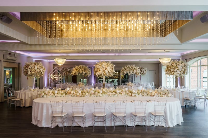 a long table set up for a wedding breakfast with white draped backdrop and tall floral centrepieces.
