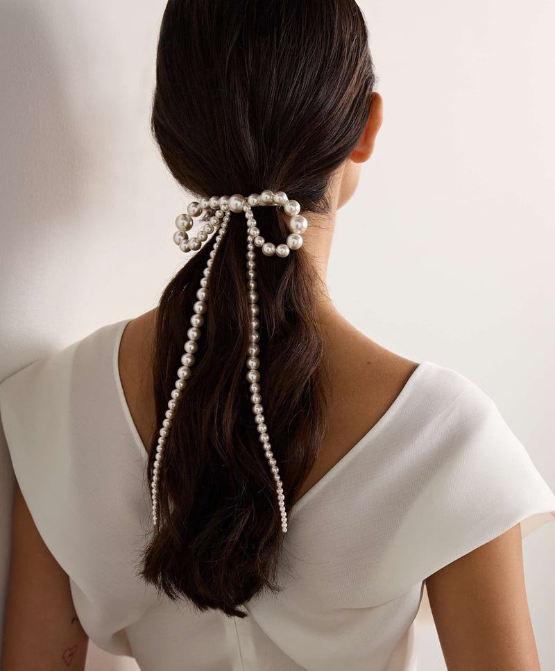 a brunette model wears a low ponytail and a pearl bow-shaped clip in the back.