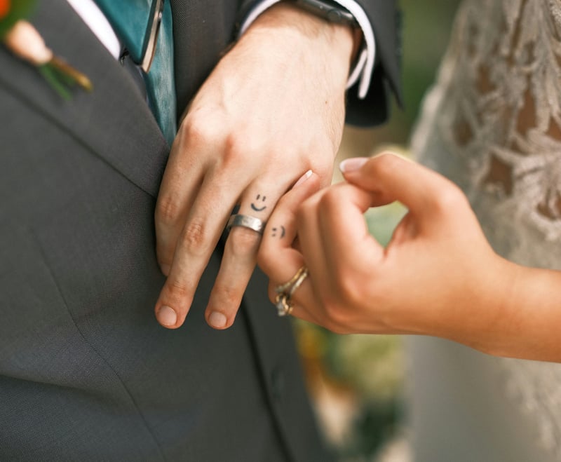 close up of a bride and groom's hands showing their wedding rings and matching smiley face tattoos on their fingers.