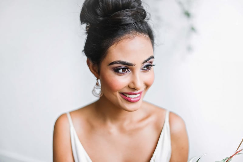 an Indian bride with beautiful makeup and her hair in a high bun smiles as she looks into the distance.