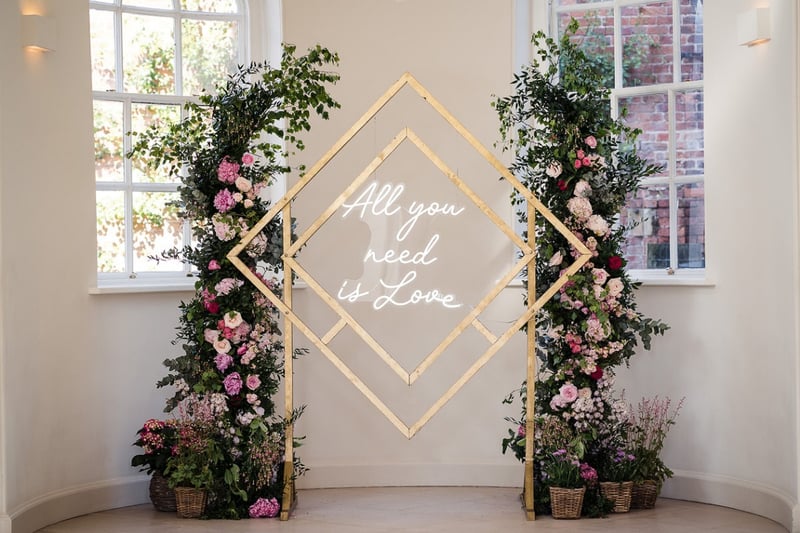 a geometric-style backdrop that reads, 'all you need is love' with floral arrangements either side.
