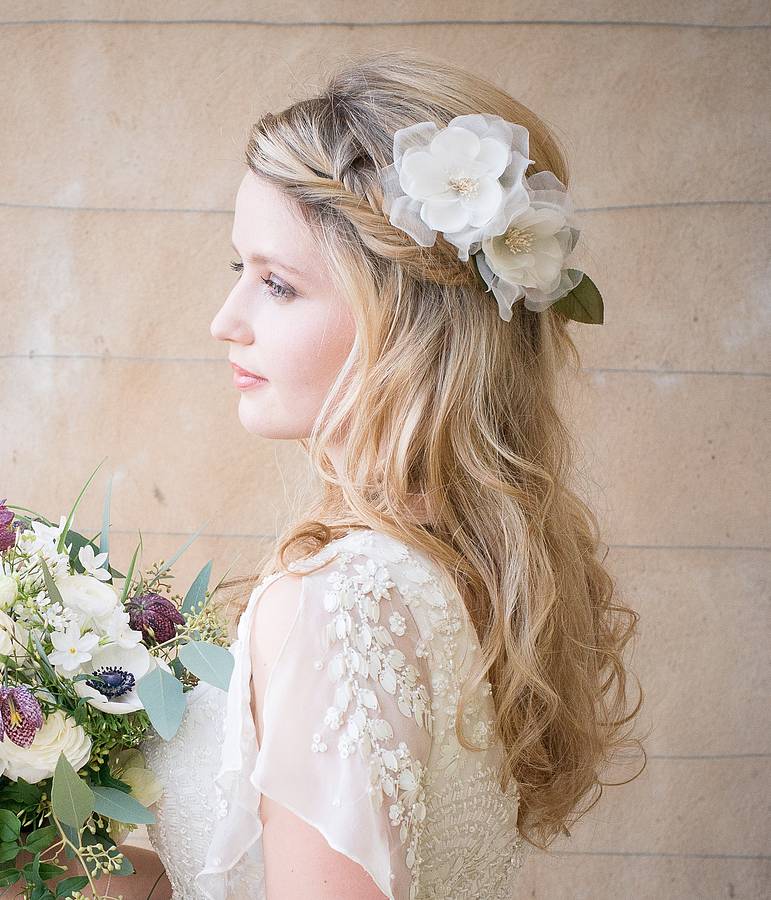 a model with long blonde wavy hair wears silk white flowers behind one ear.