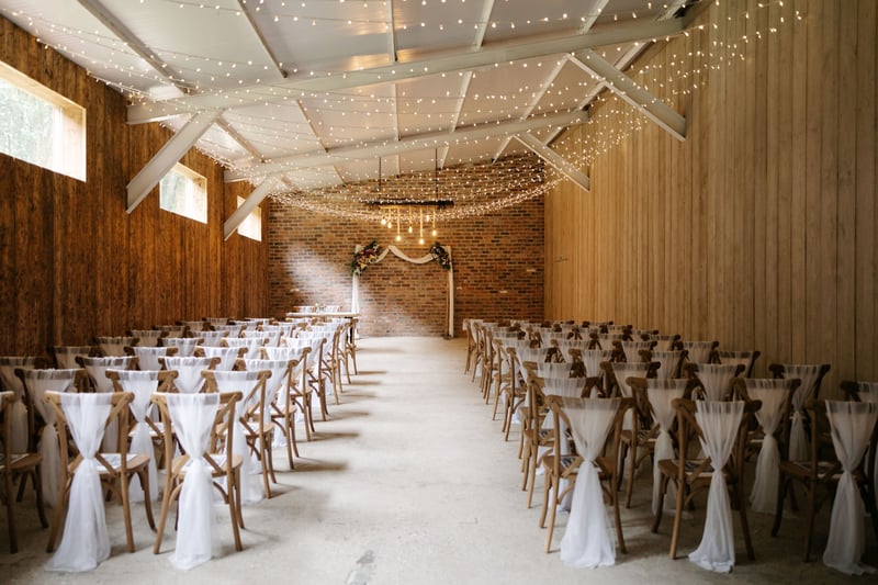 interior of a barn wedding venue in Yorkshire set up for a ceremony with fairy lights on the ceiling.