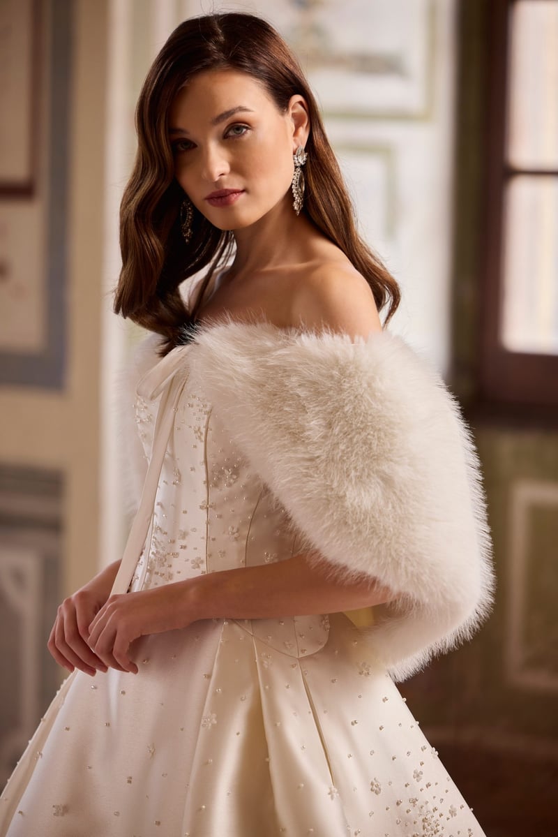 a model wears a white embellished wedding dress with faux fur wrap.