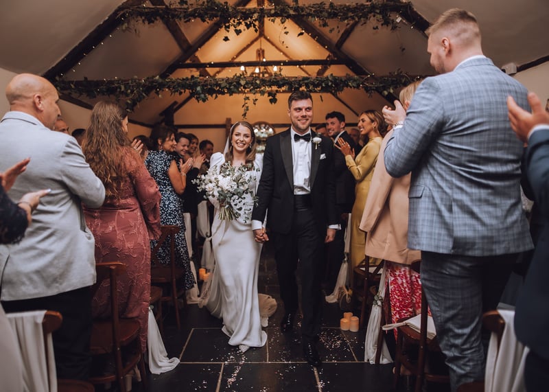 a bride and groom walk up the aisle at their winter wedding as guests clap from their seats.