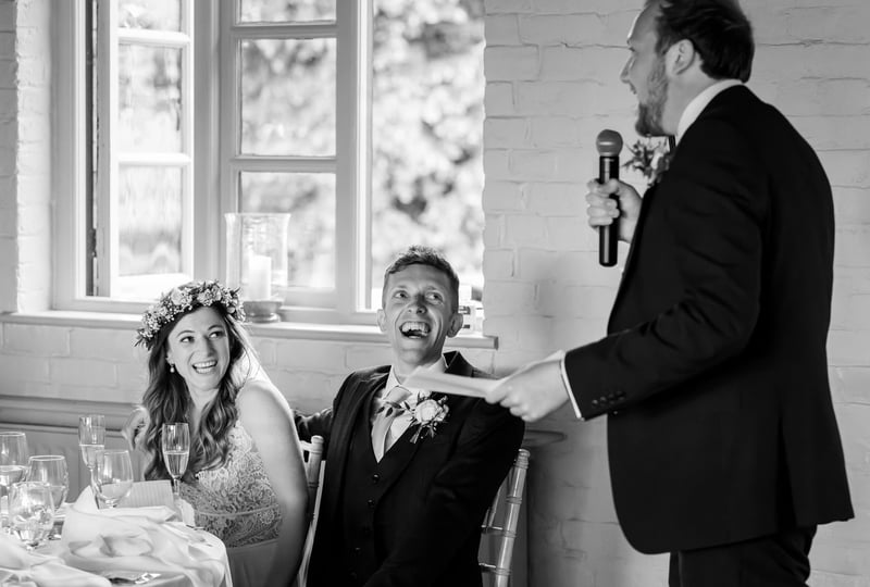 a best man giving a speech as the bride and groom laugh from the top table.