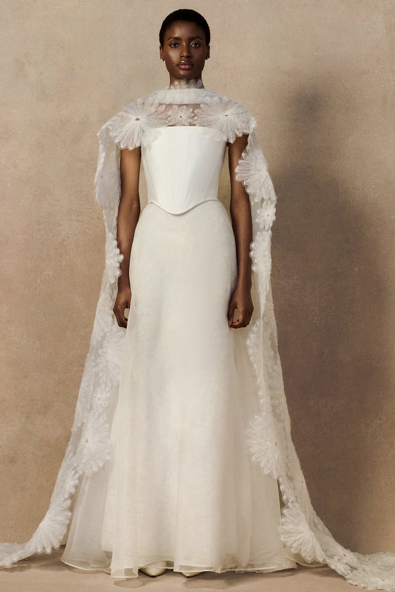 a black model wears a floor-length cape made in organza with looped daisy motifs in raw-edged silk organza with bridal separates. 